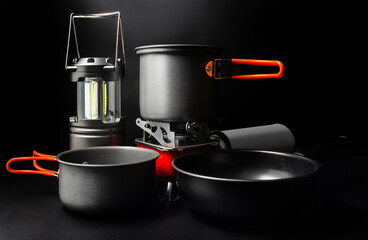 Photo of titanium camping cookware with led lantern and portable gas stove on black backdrop.