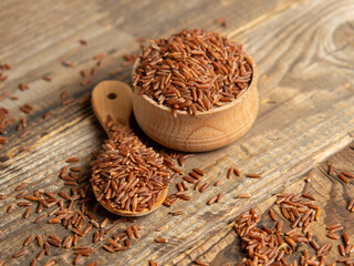 Red rice (brown rice) in a wooden bowl, red rice scattered on the ground.close up