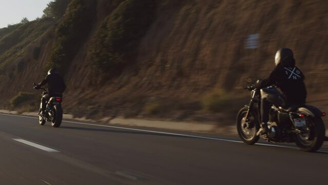Motorcyclists riding beautiful bikes along a coastal highway. Back view of the bikers driving within cinematic mountainous landscape in California. High quality 4k footage