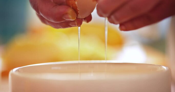 Cracking an uncooked raw egg, spilling the wite and the yolk into a cooking bowl, slow motion