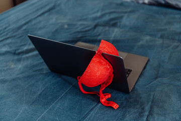 Female lace red bra on laptop on a bed. Concept of sex after work at home during COVID-19 pandemic