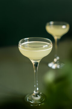Citrus alcoholic cocktails. Two drinking glasses of gimlet cocktails on minimalistic dark green background. Selective focus.