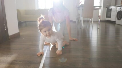 Crawling funny baby girl in bodysuit she is heading for her mother. creeping on floor at home. Infant baby plays with family in the house and learns how to crawl quickly during catch up games