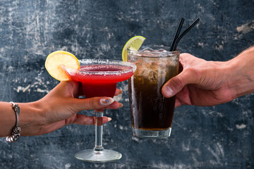 Red margarita cocktail and Rum and Cola Cuba Libre cocktail in a woman's hand