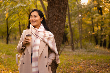 Attractive fashionable business woman taking a coffee break in a forest park with yellow and orange color autumn leaves.
