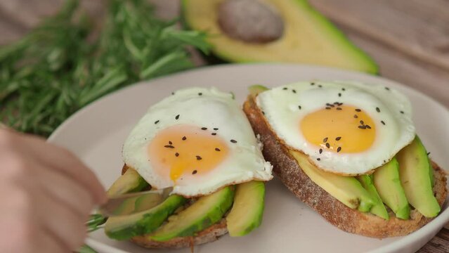 Spreading Yolk Two Toasts avocado fried egg, rosemary. 4K Preparing healthy toast breakfast with avocado slices rye wholegrain bread and sunny side up egg on top. Healthy breakfast for two, couple