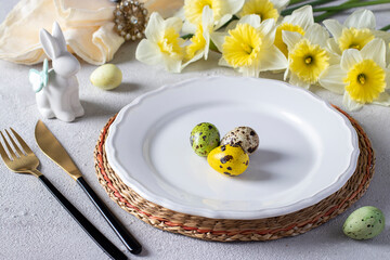 Easter table setting with daffodils, quail eggs and bunny on light gray table. Elegance dinner