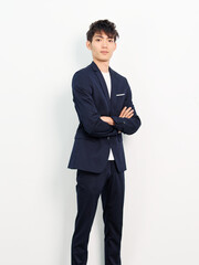 Obraz na płótnie Canvas Portrait of handsome Chinese young man in dark blue leisure suit posing against white wall background. Arms crossed and looking at camera, looks confident.