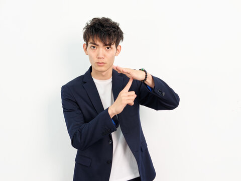Portrait of handsome Chinese young man in dark blue leisure suit posing against white wall background. Finger point to palm to make stop gesture.