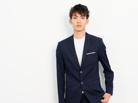 Portrait of handsome Chinese young man in dark blue leisure suit posing against white wall background. Hand in pocket looking at camera, looks confident.