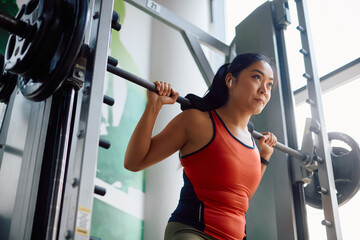 Asian athletic woman doing back exercises with barbell during sports training at gym.