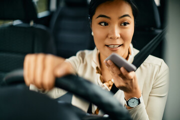 Young Asian woman sends voice message via smart phone while driving car.
