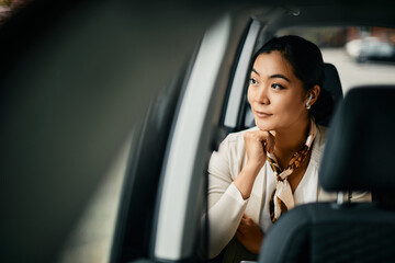 Smiling Asian female CEO looks through window while going on business trip by car.