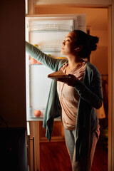 Young Asian woman takes food out of the fridge in the kitchen at night.