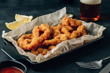 Rings of squid with lemon on a black background. Snack to beer.