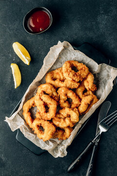 Rings of squid with lemon on a black background. Snack to beer.