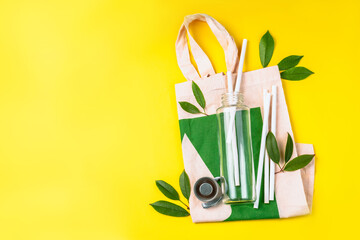 The concept zero waste.Life without Plastic.Reusable glass bottle for water on yellow background.May bottle.Cotton bag,glass bottle and bamboo tubes.Let's go shopping.Ecological, natural materials.