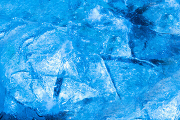 Close up photo of blue toned frozen cracked and damaged ice surface texture.