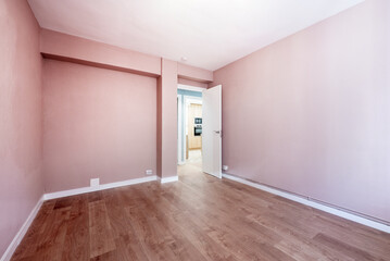 Empty room painted with pastel pink paint, wooden floor, white wood carpentry and white wooden door