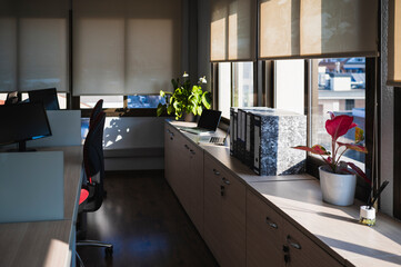 Empty office illuminated by natural light with several work desks.