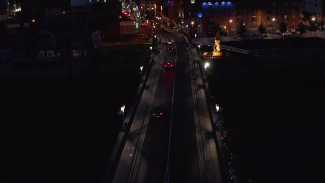 Forwards tracking of cars driving on road bridge across Shannon river. Aerial view of streets in night city. Limerick, Ireland