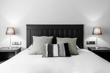 Black wooden headboard with matching bedside tables, lamps with translucent black lampshade, white quilt and gray cushions