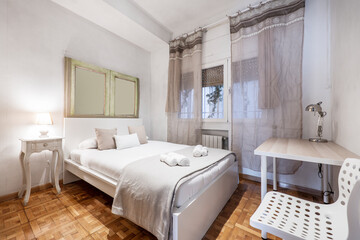Fototapeta na wymiar Bedroom with king size bed, wooden headboard and mirror, translucent curtains, study table and matching wooden side tables