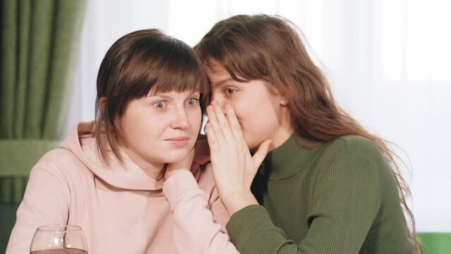 Young cute woman whispering secret on ear to her female friend. Communication and surprised girl by gossip.
