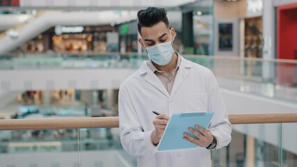 Young arab security inspector keep records checks correctness hispanic supervisor with medical mask and robe inspecting shopping mall controller writes statistical data observer conducting research