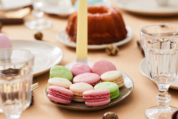 Fototapeta na wymiar Closeup of pastel macaroons platter on elegant dinner table decorated for Easter and Spring, copy space