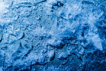 Photo of blue toned frozen cracked ice with snow particles surface texture.