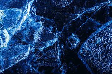 Photo of blue toned frozen cracked ice pieces surface texture on dark backdrop.