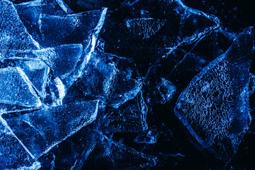 Photo of blue toned frozen cracked ice pieces surface texture on dark backdrop.