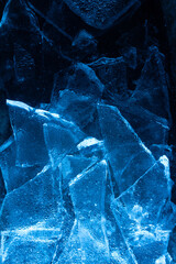 Photo of blue toned frozen cracked ice pieces surface texture on dark backdrop.