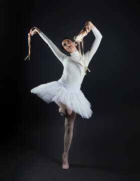 joyful ballerina barefoot, holding pointe shoes in her hands. photo shoot in the studio on a dark background