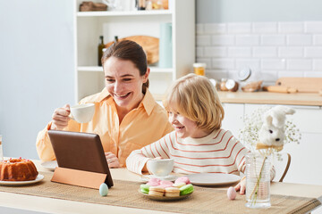 Portrait of happy mother enjoying breakfast with cute son and using tablet in kitchen, copy space