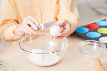 Close up of young woman breaking eggs while baking homemade muffins in kitchen, copy space