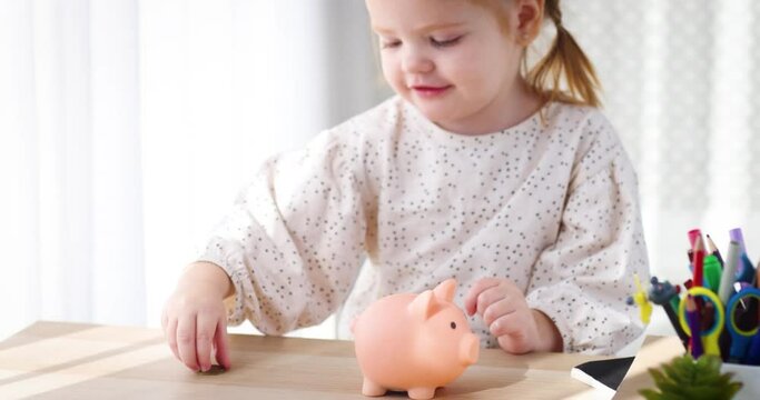 Getting your child into saving from an early age. happy toddler baby girl drops coins into the piggy bank. Teaching your kid to plan the budget with money box