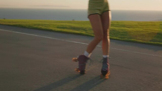 Young active woman skating on rollers by the beach and ocean. Female sporty athlete dances at playground on golden hour with sun setting in the background. High quality 4k footage