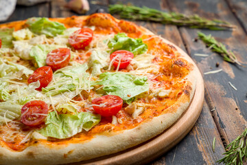 Pizza Caesar with chicken, salad and tomatoes on old wooden table macro close up
