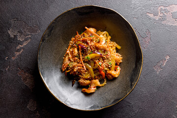 wok with shrimp and vegetables on black bowl on dark stone table top view