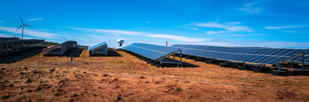 Clean energy installation or solar wind energy station. Photo-voltaic cell panels, a wind turbine, a water tank over the dried green field of wilderness.
