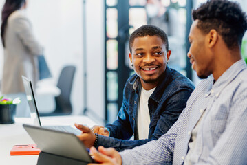 two black men work together on a project with a digital tablet in an office. two young african...