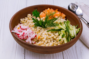 Pearl barley with vegetables on bowl on white wooden table