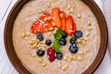 amaranth porridge with fresh berries,nuts and mint on brown bowl on white wooden table top view macro close up
