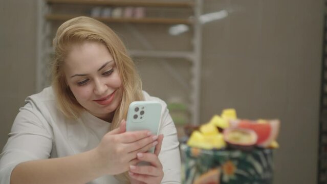 Young blonde woman taking photo of rotating cake decorated with mango, passion fruit, grapefruit and blueberry. Bakery process in slow motion.