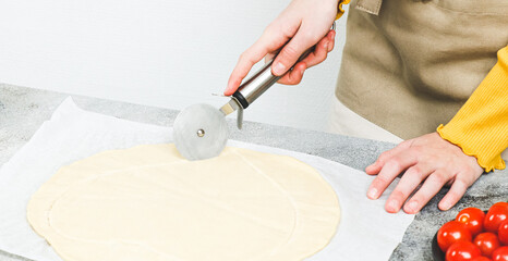 Hands of a caucasian teenage girl in an apron cut out the dough in the shape of a heart for pizza.