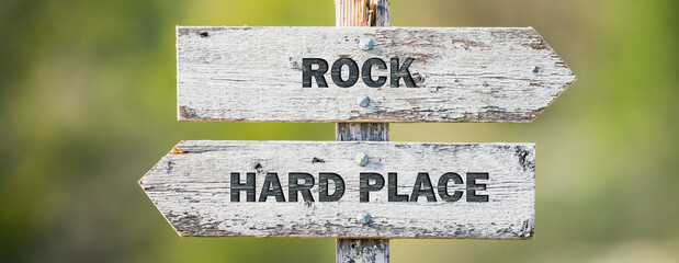 opposite signs on wooden signpost with the text quote rock hard place engraved. Web banner format.