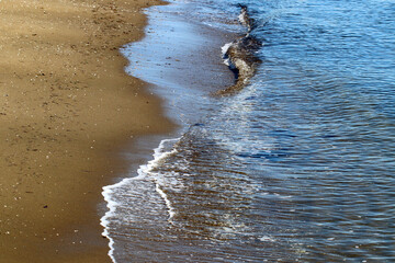 Beige brown sand beach with swash zone. 茶色い砂浜の静かな波打ち際の写真。