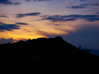 Man walking on top of a mountain looking at the sunset